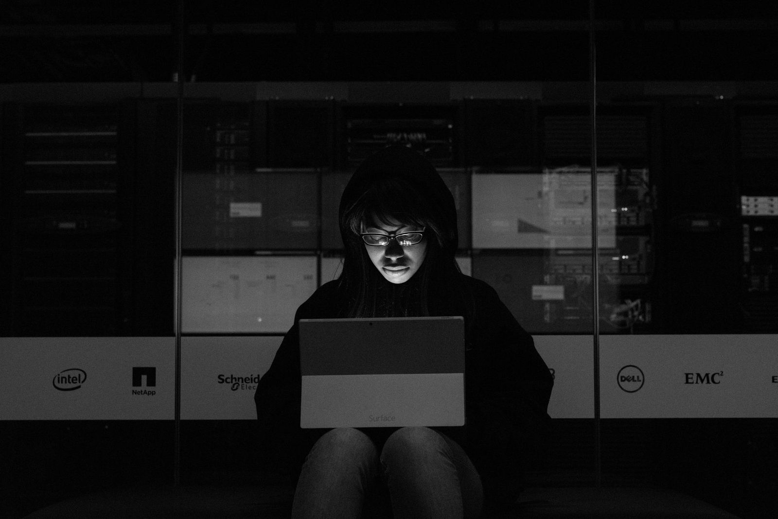 Foto in bianco e nero di una persona con il cappuccio che usa un computer portatile in una stanza buia