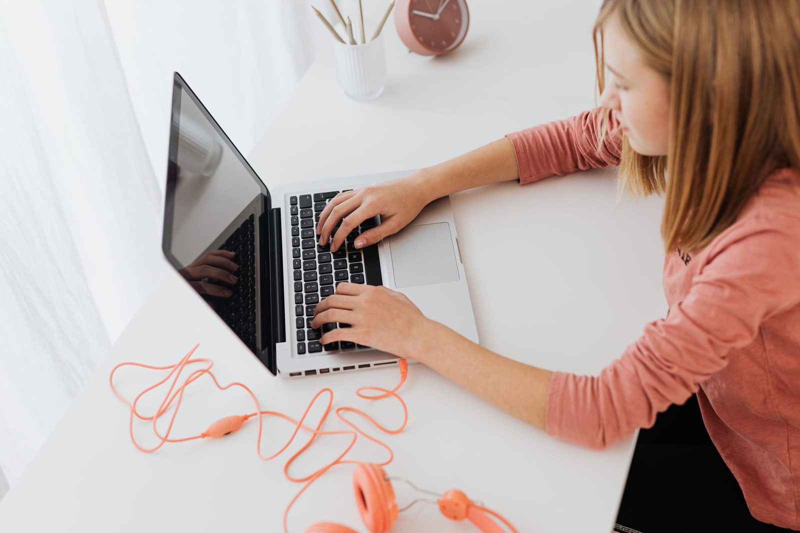 Jeune femme tapant sur un ordinateur portable posé sur un bureau blanc, casque audio orange à côté