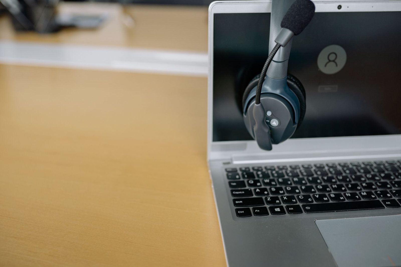 Headset resting on the screen of an open laptop, on a light wooden desk