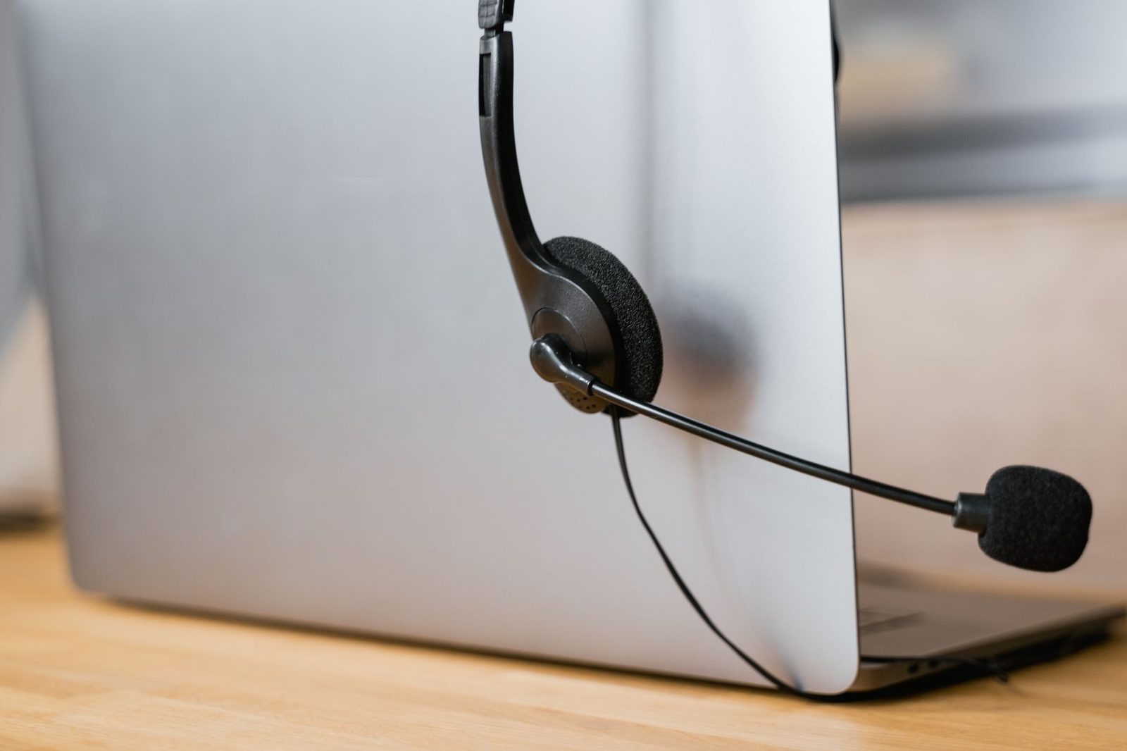 Black headset leaning against a closed silver laptop on a light wooden desk