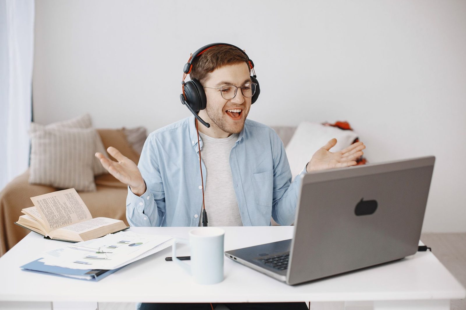 Homme souriant avec casque-micro en visioconférence devant un ordinateur portable à un bureau blanc