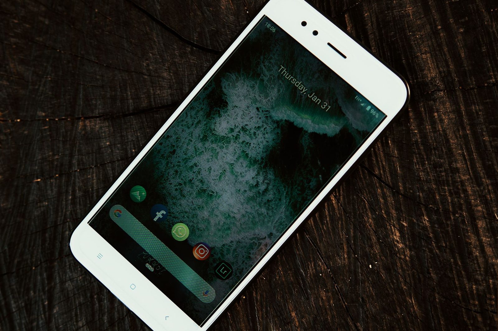 Smartphone blanc posé sur un bois sombre, écran d'accueil allumé avec icônes d'applications