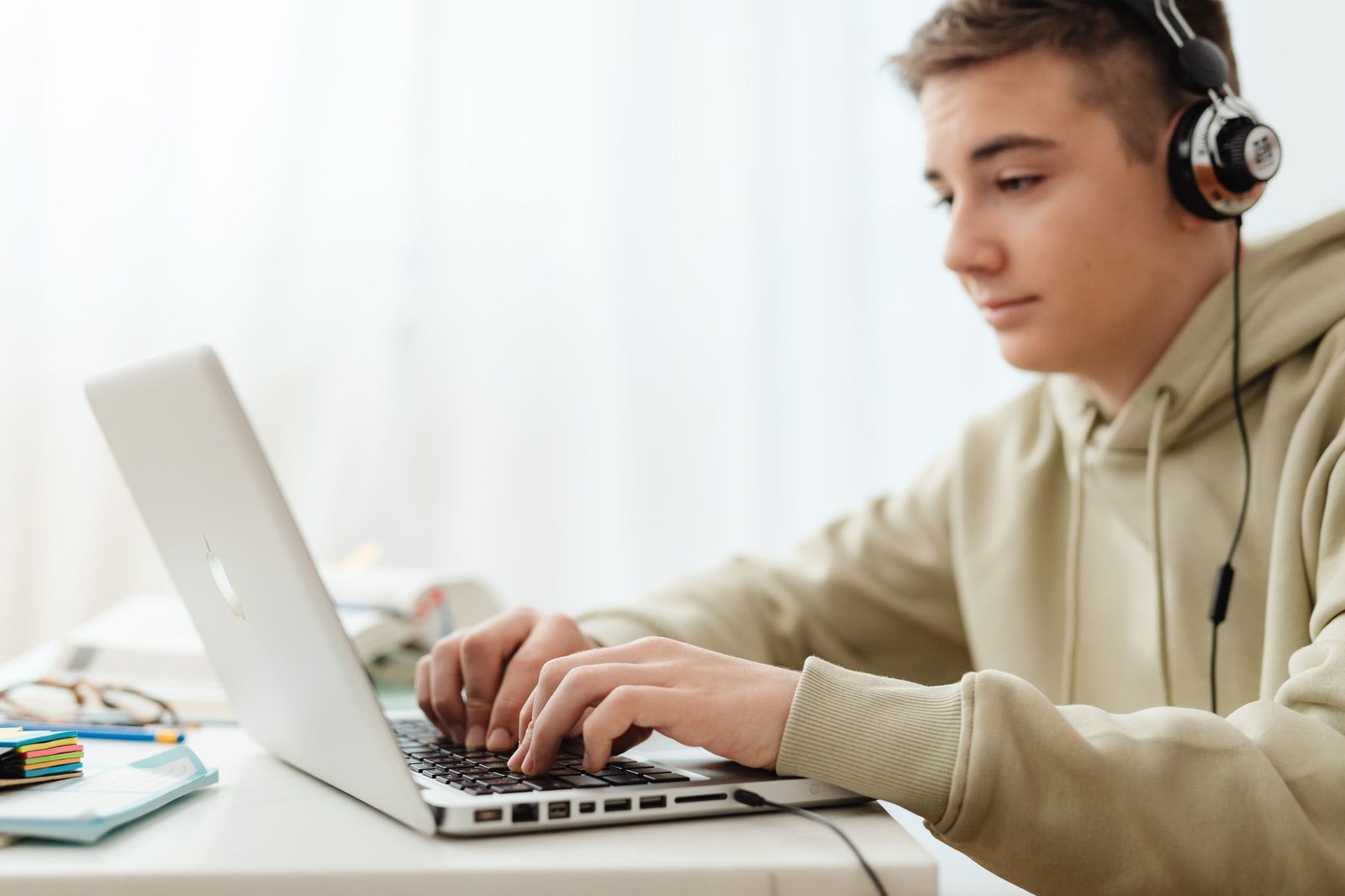 Adolescent avec un casque audio tapant sur un ordinateur portable assis à un bureau clair