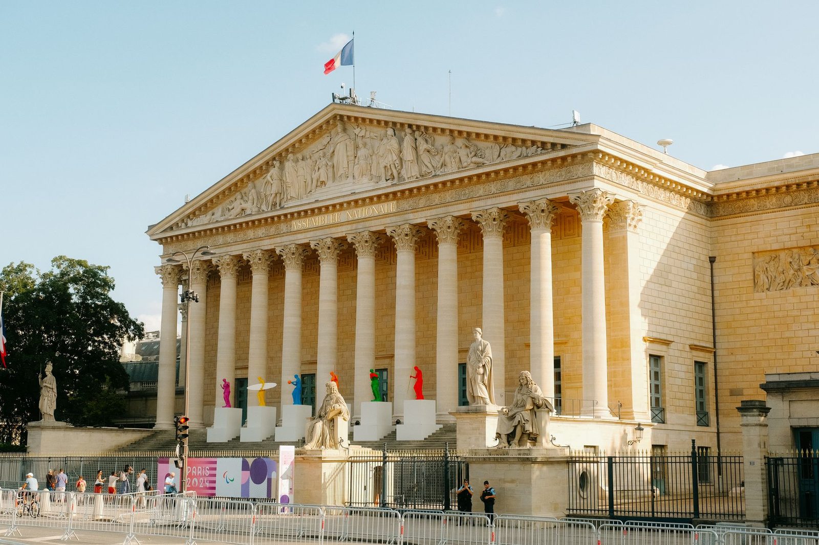 Façade de l'Assemblée nationale à Paris avec drapeau français, colonnes et passants derrière des barrières