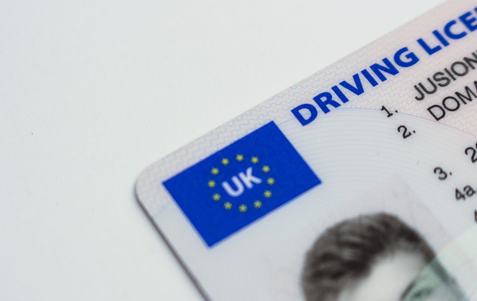 Gros plan sur un permis de conduire britannique posé sur fond blanc, avec drapeau UK et photo d'identité