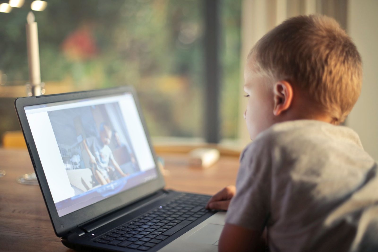Jeune enfant de dos devant un ordinateur portable posé sur une table, regardant une vidéo à l'écran