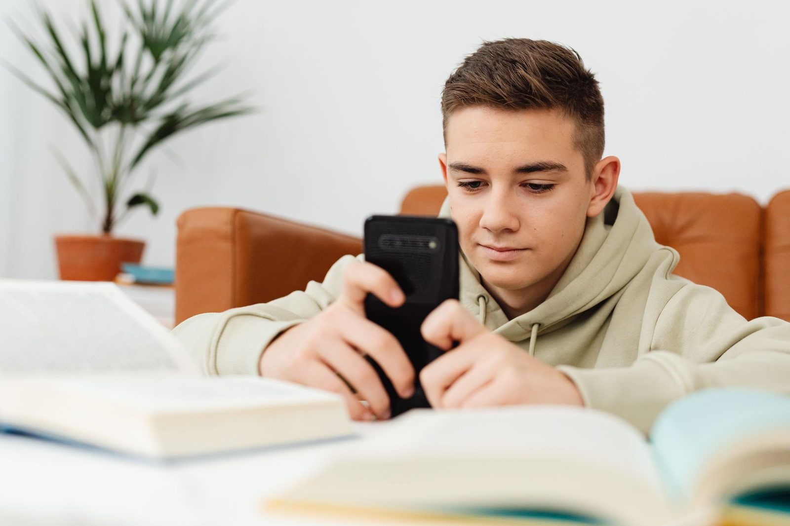 Adolescent utilisant un smartphone devant des livres ouverts sur une table