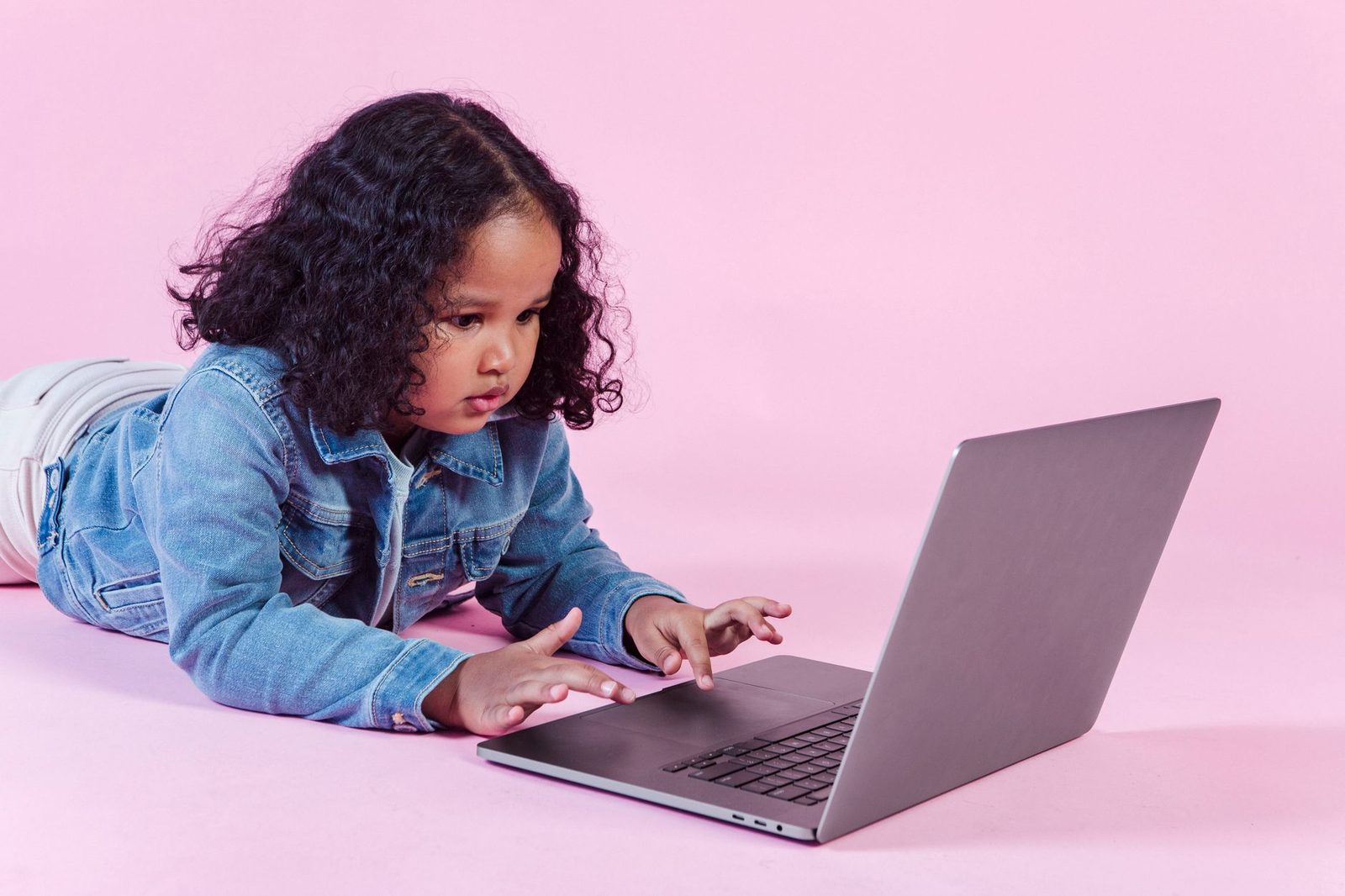 Jeune enfant allongé au sol utilisant un ordinateur portable sur fond rose