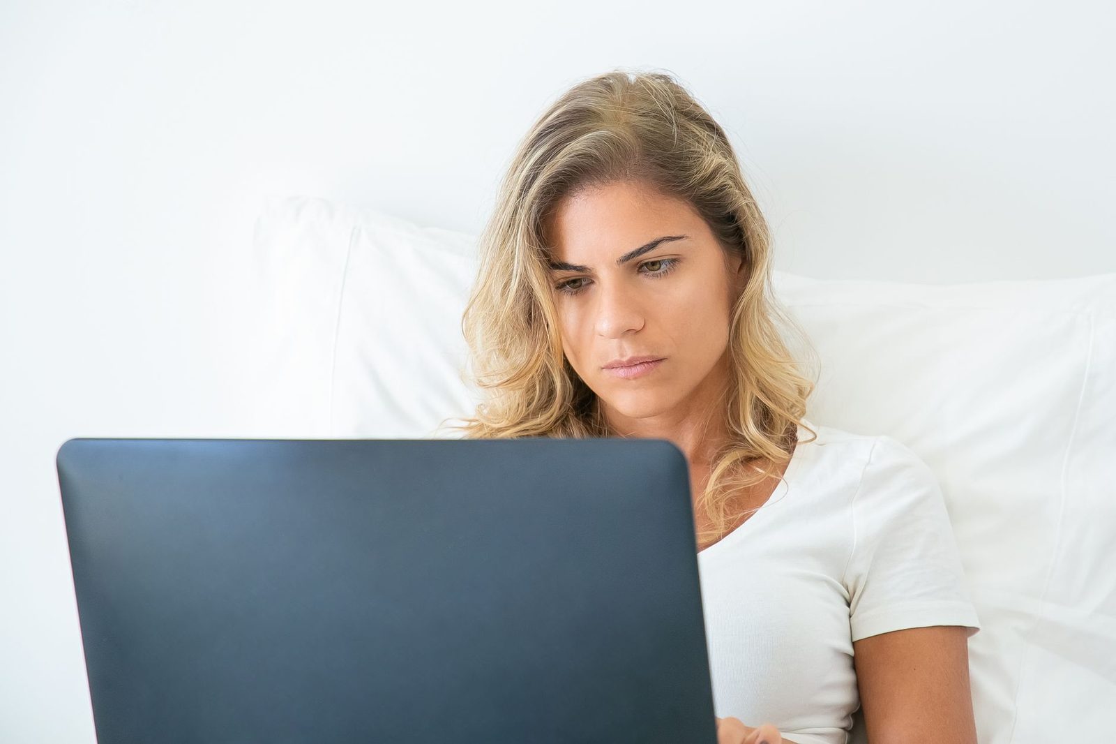 Jeune femme blonde allongée sur un lit, concentrée devant l'écran d'un ordinateur portable